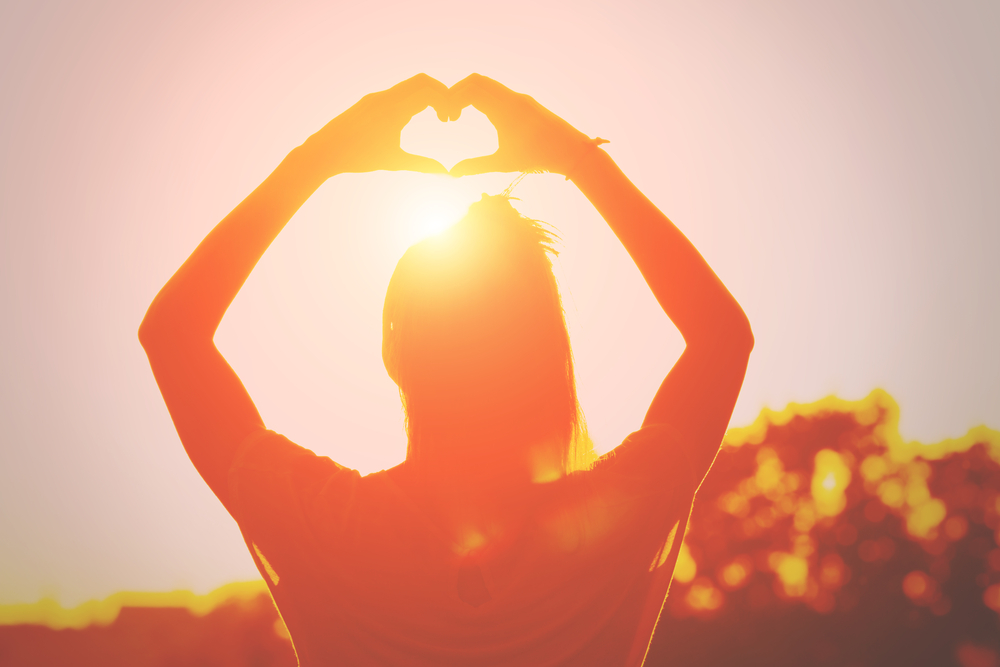 Myasthenia Gravis News | Stock photo of a woman making a heart sign with her hands in the direction of the sun