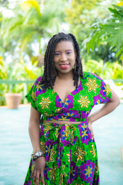 A woman poses for a photo outside amid palm trees in Puerto Rico. She's wearing a matching top and skirt, both featuring green, purple, blue, and yellow flowers.