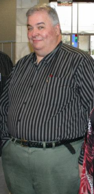 A photo shows a man before he developed myasthenia gravis. He's wearing a striped long-sleeved shirt, slacks, and a black belt.