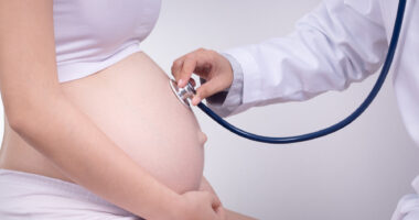 photo of a pregnant women being examined by doctor putting a stethoscope on her stomach