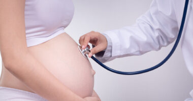 photo of a pregnant women being examined by doctor putting a stethoscope on her stomach