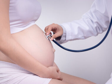 photo of a pregnant women being examined by doctor putting a stethoscope on her stomach