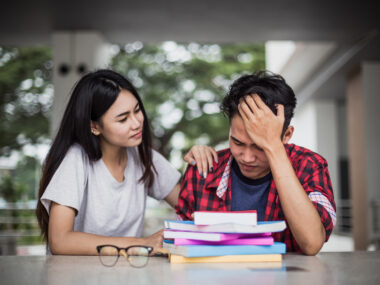 Woman sitting at table consoling tired man with head in his hands