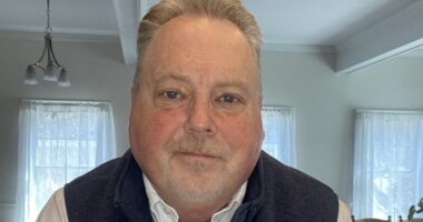 A face shot of a man sitting in his living room, taken from the camera on a computer.