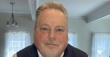 A face shot of a man sitting in his living room, taken from the camera on a computer.