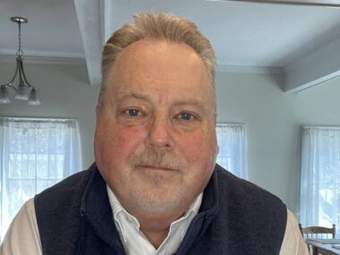 A face shot of a man sitting in his living room, taken from the camera on a computer.