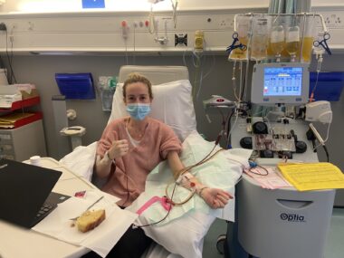 A woman wearing a face mask lies in a hospital bed receiving intravenous treatment.