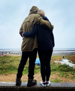 A man and a woman stand on a wall facing a beach