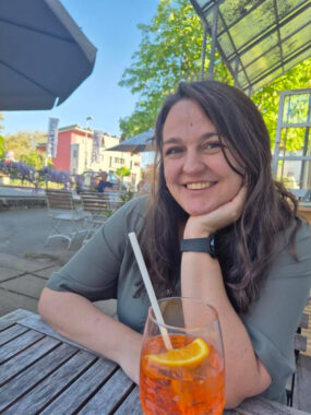 Retha De Wet sits outside at a table with a beverage in front of her.