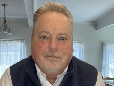 A close-up head shot of a man in his home, taken on computer camera.