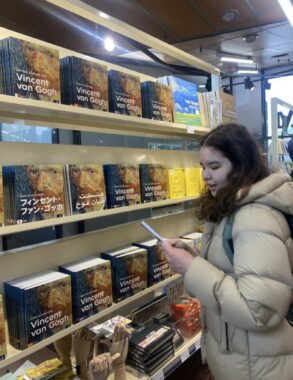 A young woman in a puffy jacket browses in a store. The shelves are lined with books about Vincent van Gogh.
