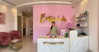 A woman stands behind a reception desk at a pink-themed aesthetician's clinic.