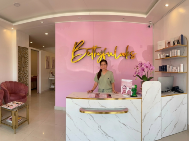 A woman stands behind a reception desk at a pink-themed aesthetician's clinic.