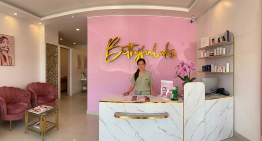 A woman stands behind a reception desk at a pink-themed aesthetician's clinic.