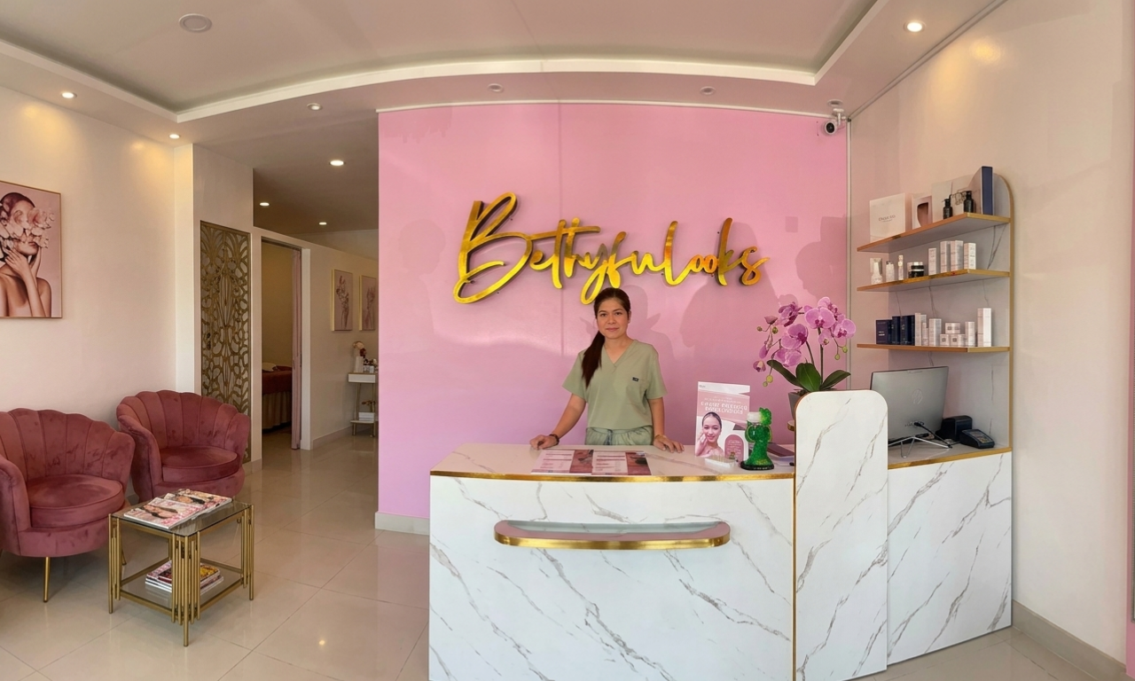 A woman stands behind a reception desk at a pink-themed aesthetician's clinic.