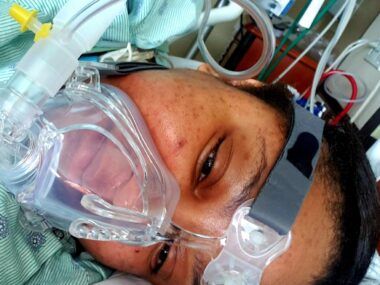 A woman lies in a hospital bed with an oxygen mask covering her nose and mouth.