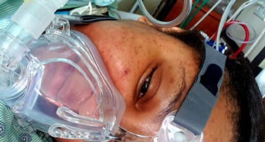 A woman lies in a hospital bed with an oxygen mask covering her nose and mouth.