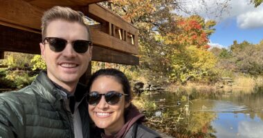 A couple wearing sunglasses take a selfie while on a walk outdoors.