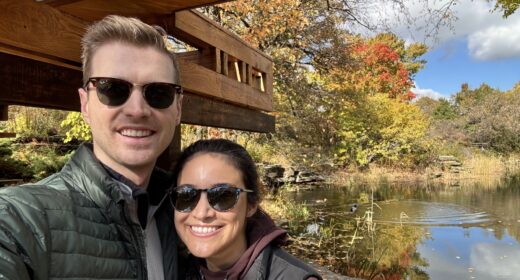 A couple wearing sunglasses take a selfie while on a walk outdoors.