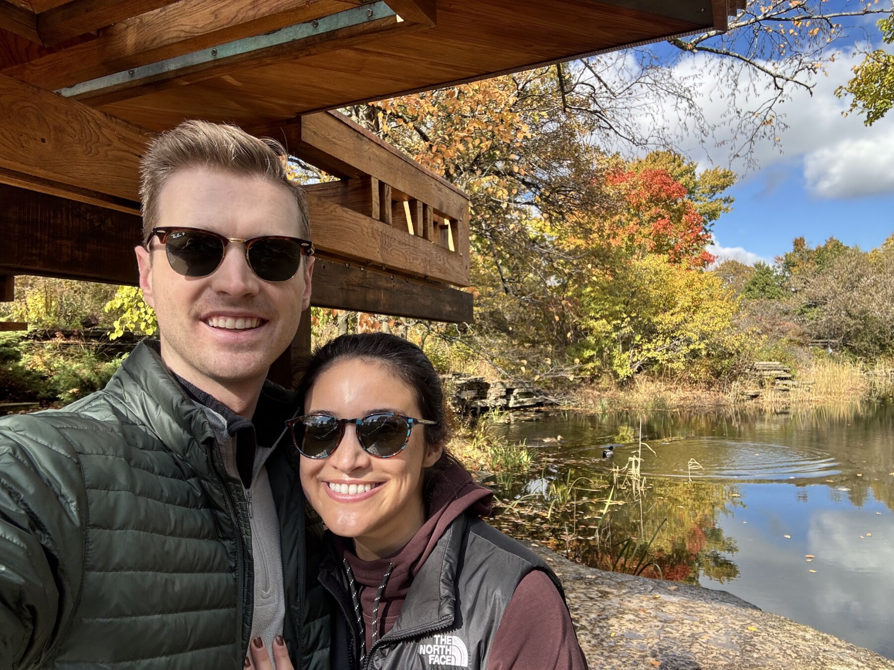 A couple wearing sunglasses take a selfie while on a walk outdoors.