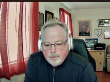 A man wearing headphones is seen working in a home office.