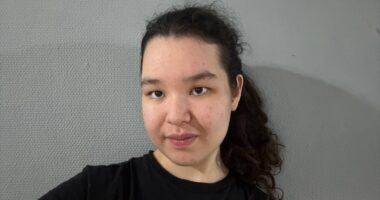 A woman in a black T-shirt takes a selfie.