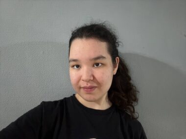 A woman in a black T-shirt takes a selfie.
