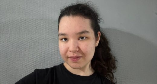 A woman in a black T-shirt takes a selfie.
