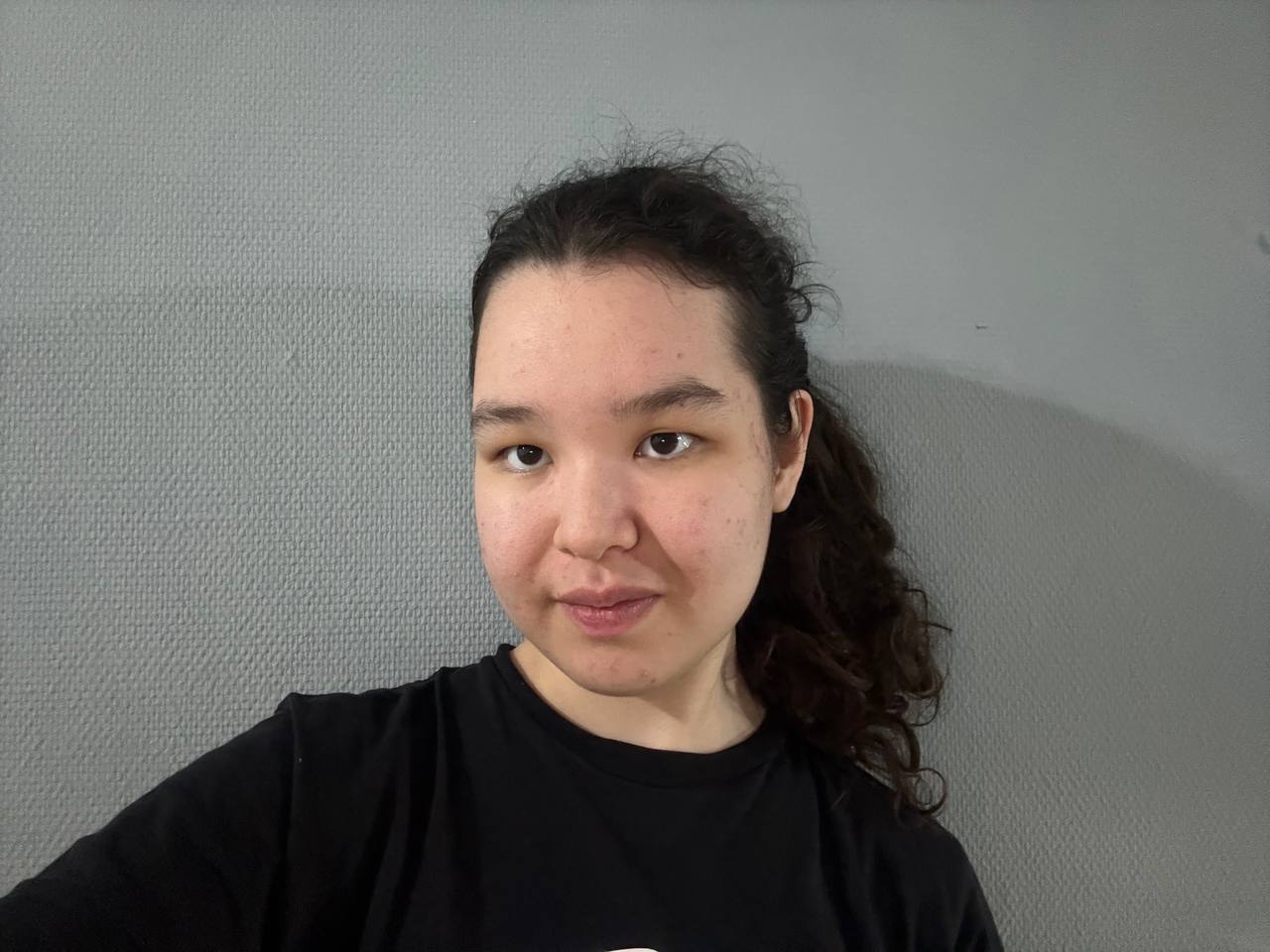 A woman in a black T-shirt takes a selfie.