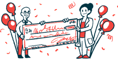 Two people, flanked. by balloons, hold an oversized check.